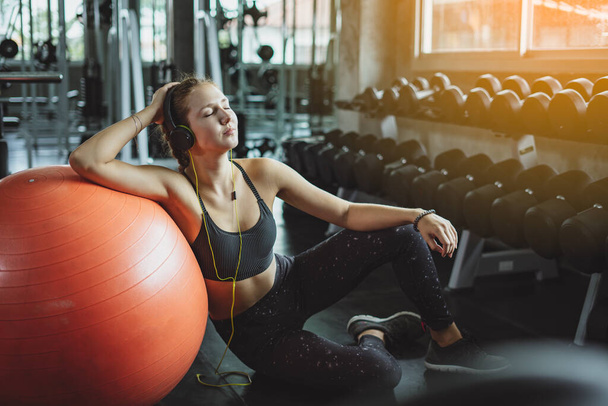 Young woman with earphones listening to music after hard workout in gym. Relax concept. Strength training and Body build up theme. Warm and cool tonePretty girl scrolling in her mobile phone. Close up - Foto, Bild