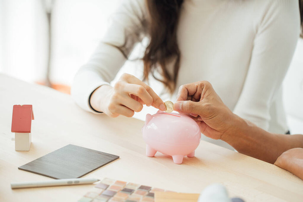 Üzletember tesz egy érmét egy rózsaszín malac bank koncepció megtakarítás és pénzügy.Pár álmodik az új otthon. - Fotó, kép