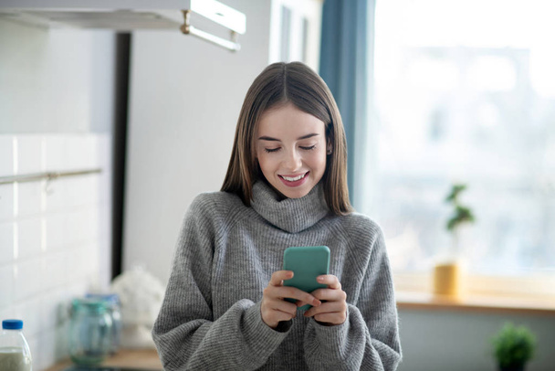 Dark-haired girl in a grey sweater typing a message - Foto, Bild
