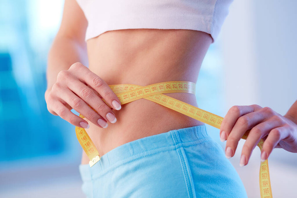 Close-up of a fit female with slim waist and a measuring tape - Foto, Imagem