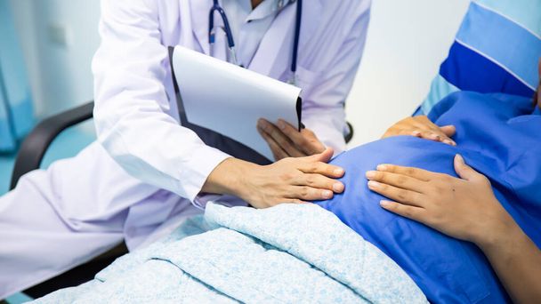 Pregnant Woman Being Given Ante Natal Check By Doctor Holding Clipboard Looking At Notes.Pregnant women and male doctor with stethoscope. - 写真・画像