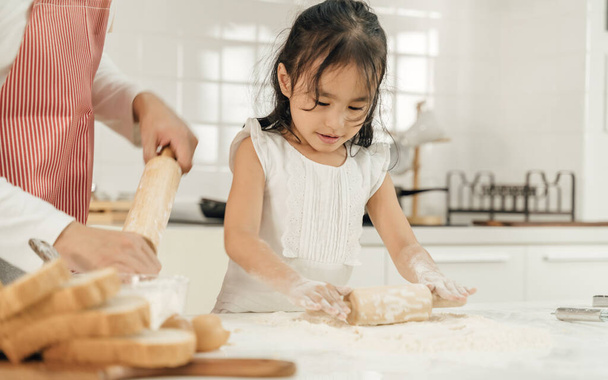 Young asian family cooking food in kitchen.Happy Little girl with her father and mother mixing batter.mother and Little girl preparing the dough.Happy family in the kitchen and junior chef Concept. - Фото, изображение