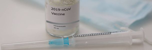 Флакон с вакциной 2019-nCoV стоит на столе с пустым шприцем
 - Фото, изображение
