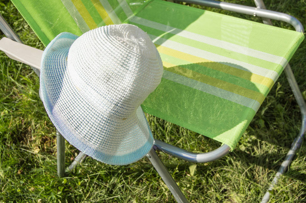 One empty folding garden chair for relaxing stands on the green grass on the lawn on a Sunny summer day, a copy of the space, a hat hanging on the chair - Photo, image