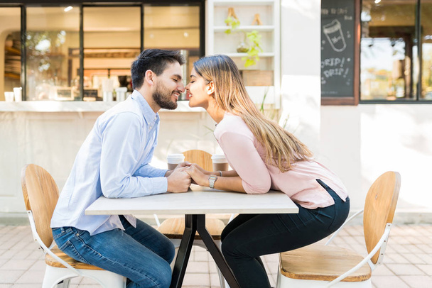 Улыбающиеся влюблённые мужчина и женщина держатся за руки в кафе на тротуаре
 - Фото, изображение