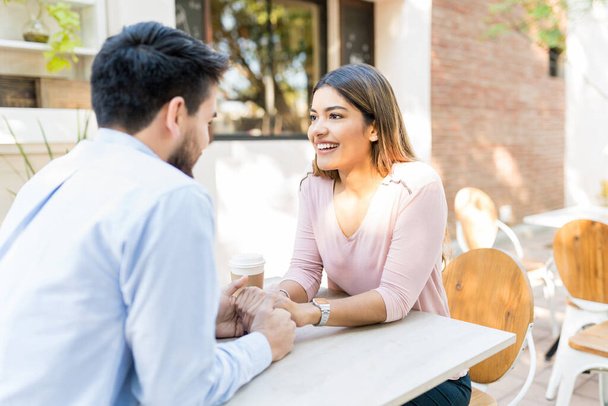 Счастливая девушка, держась за руки парня, сидя в кафе на тротуаре
 - Фото, изображение