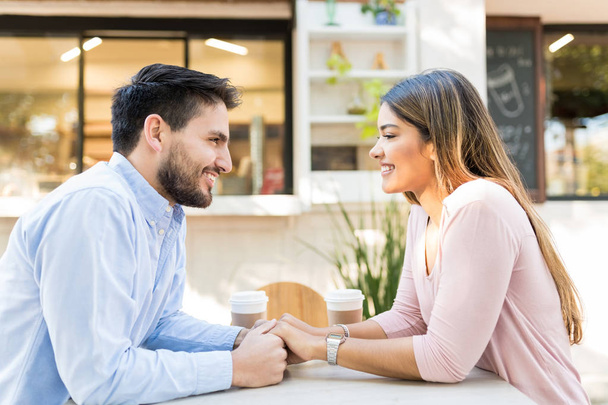 Vista lateral de novio y novia felices tomados de la mano mientras están sentados en el café de la acera
 - Foto, imagen