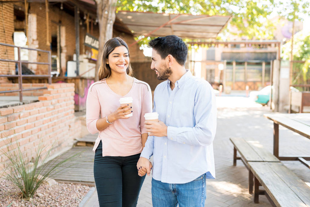 Щасливий хлопець і дівчина тримають одноразові чашки кави під час прогулянки пішки за межами кафе
 - Фото, зображення