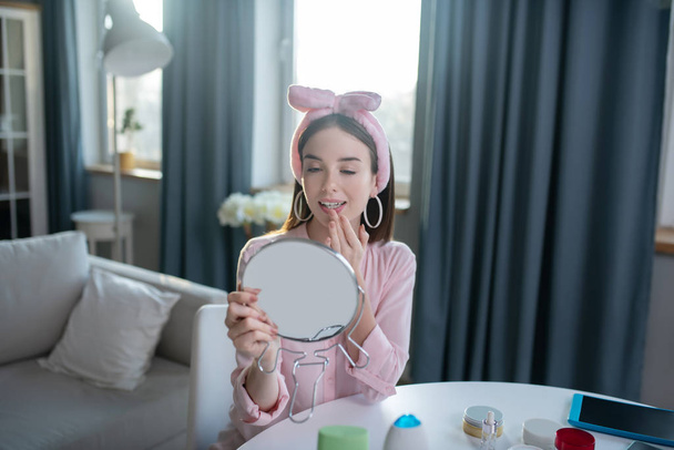 Smiling pretty girl in a pink headband looking in the mirror - Φωτογραφία, εικόνα