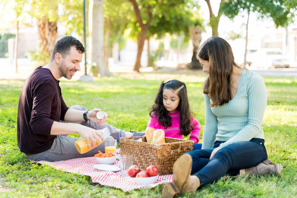 Mother And Daughter Looking At Man Pouring Juice During Picnic At Park - Photo, Image