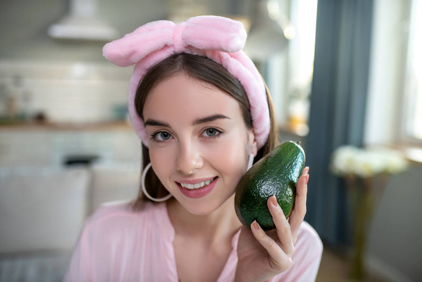 Young pretty girl in a pink headband holding avocado in her hand - Фото, зображення