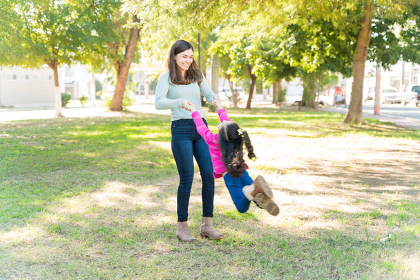 jong Moeder genieten met dochter terwijl swinging haar in park - Foto, afbeelding