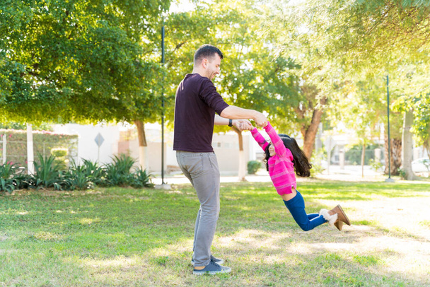 Side View Of Man Swinging Girl While Standing At Park On Sunny Day - Photo, Image