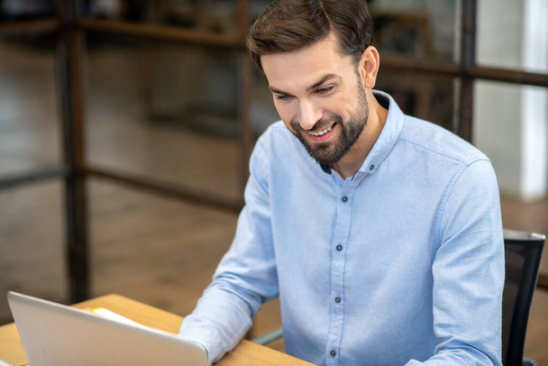 Young bearded man sitting at the laptop and smiling - Foto, Imagem