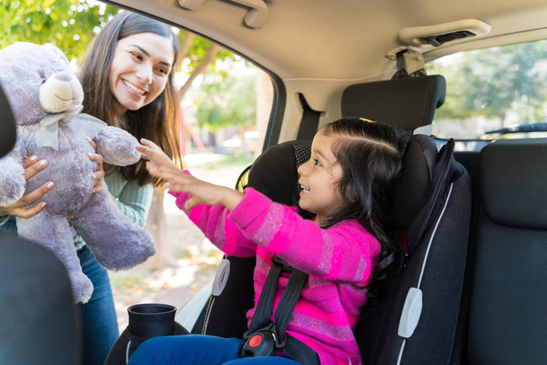 Cheerful Young Mother Giving Teddy Bear To Excited Girl Sitting In Car - Foto, Bild