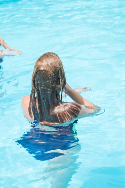 Happy girl with wet hair standing in the water in an outdoor pool, having fun in the water on vacation, vertical photo, back view - Foto, Imagem