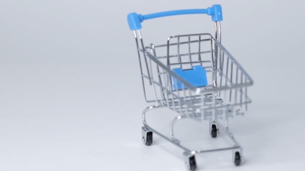 Einkaufsspielzeugwagen auf weißem Hintergrund mit etwas Kopierraum. Online-Shopping-Konzept Nahaufnahme Zeitlupe. - Filmmaterial, Video