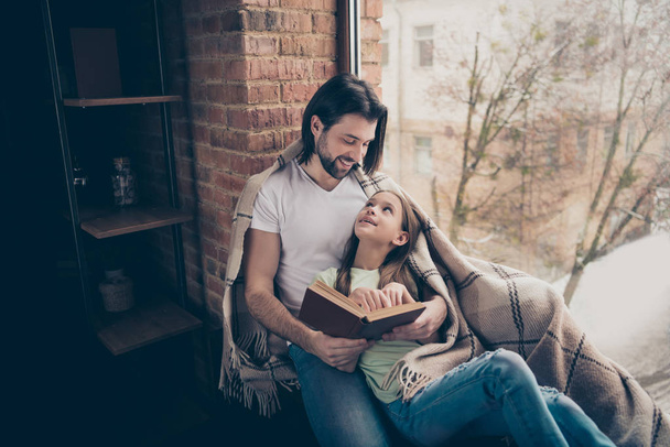 Photo of little adorable pretty lady and her handsome young daddy reading book fairy tale sit window sill spend weekend time homey atmosphere covered blanket house room indoors - Foto, afbeelding