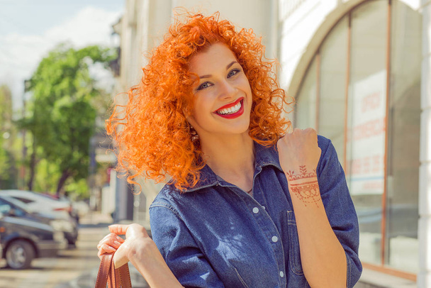 Happiness, winner. Portrait smiling beautiful city lifestyle woman looking at camera raising hand pumping fist. Pretty young girl with red curly hair isolated street background. Positive expression - Фото, зображення