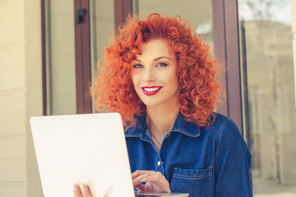 Happy daydreaming young woman holding open notebook, looking camera, smiling, sitting outdoor. Portrait of attractive pretty girl with red curly hair. - Zdjęcie, obraz
