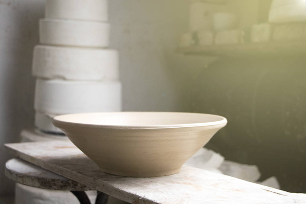 Produtos de barro, pratos cerâmicos em uma prateleira em uma oficina de cerâmica. Luz moderada e atmosfera criativa
 - Foto, Imagem