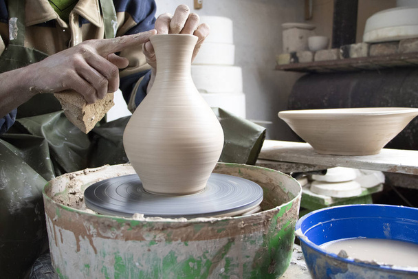 Mains d'un potier sur une roue de poterie gros plan. Ancien art traditionnel, fait main, production d'argile et de céramique. Atelier de poterie en lumière douce tamisée
 - Photo, image