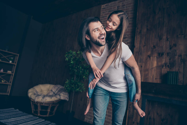 Photo of small funny energetic lady excited handsome daddy carry daughter piggyback playing games good mood spending free time together rejoicing house room indoors - Φωτογραφία, εικόνα