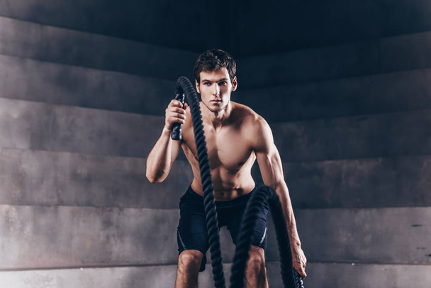 Αθλητικός νεαρός άνδρας με σχοινί κάνει άσκηση σε λειτουργική traini - Φωτογραφία, εικόνα