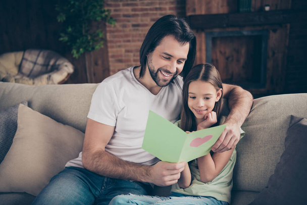 Photo of little pretty funny lady her handsome daddy sit cozy sofa hugging hold cute card birthday present reading greeting celebrate words best holiday house room indoors - Photo, image