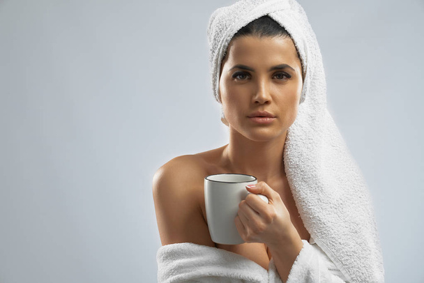 Woman in bathrobe and towel holding cup. - Valokuva, kuva