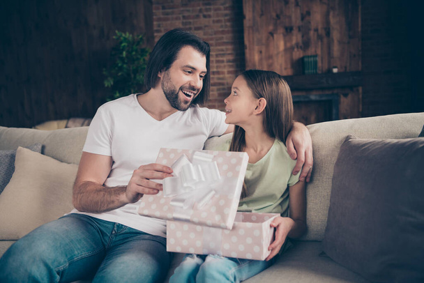 Photo of little adorable funny lady and her handsome young daddy sit cozy sofa giving receiving large giftbox unexpected birthday present celebrate domestic atmosphere indoors - Фото, зображення