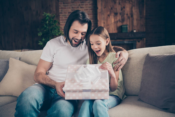 Photo of little adorable funny lady and her handsome young daddy sit cozy sofa giving receiving large giftbox birthday present gift celebrate domestic atmosphere indoors - Foto, Imagem