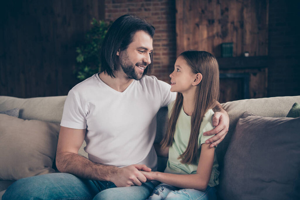 Photo of beautiful pretty little lady her handsome daddy sit comfy sofa hugging together adorable smile look eyes spending weekend time homey domestic house room indoors - Photo, Image