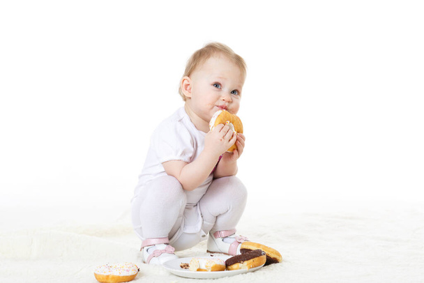 Little messy child eating doughnuts on a white background. - Photo, image
