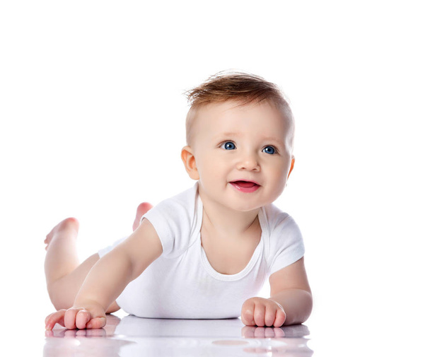 Happy smiling infant child baby boy toddler with blue eyes in white t-shirt is lying on his stomach crawling on white - 写真・画像