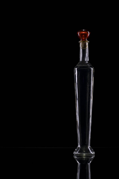 studio shot of a long narrow decoration bottle with red closure in front of black background - Foto, Imagen