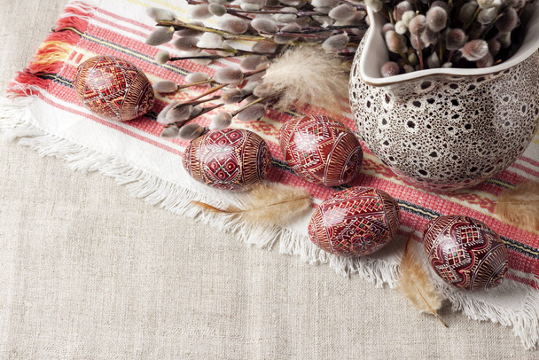 Wielkanoc martwa natura z gałęziami Pysanki i wierzby w ceramicznym dzbanku na tradycyjnej ukraińskiej tkaninie. Ozdobione pisanki, tradycyjne dla kultury Europy Wschodniej. Przestrzeń kopiowania - Zdjęcie, obraz