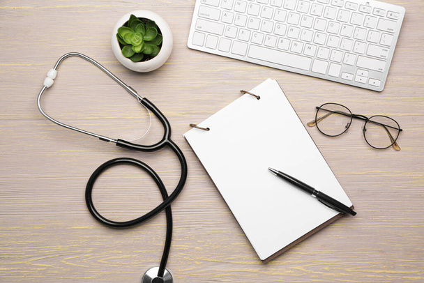 Stethoscope with computer keyboard and notebook on wooden table - 写真・画像