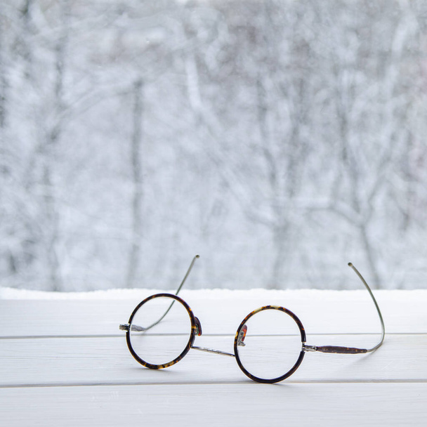 Vintage ronde leesbril op een witte vensterbank tegen de achtergrond van een bos - Foto, afbeelding