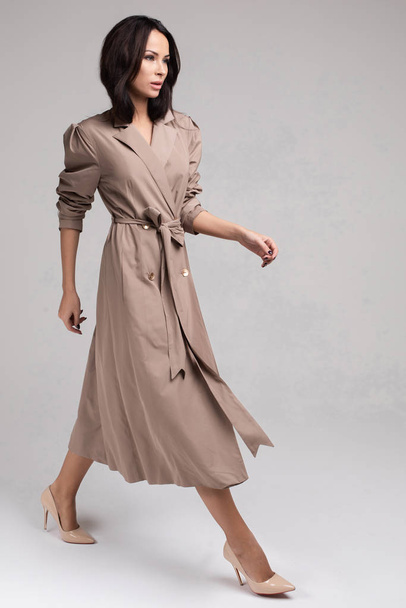 Pretty young lady in elegant trench coat walking in studio - Fotó, kép