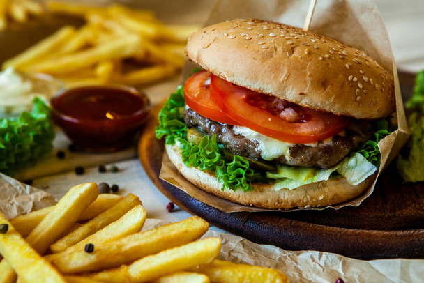 La hamburguesa grande sabrosa sobre la mesa de madera y las patatas fritas. Deliciosa hamburguesa con ternera, tomate, queso y lechuga
. - Foto, Imagen