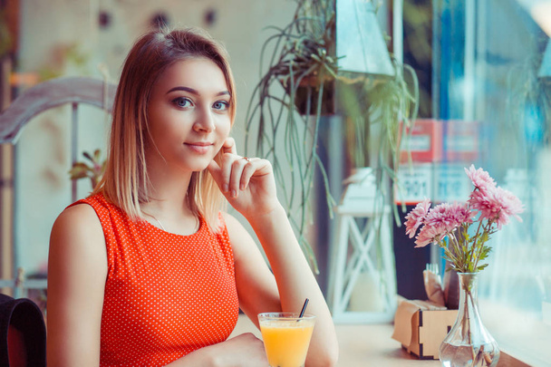 Chica feliz desayunando con jugo de naranja en una cafetería en casa cerca de la ventana y mirando a la cámara
  - Foto, imagen