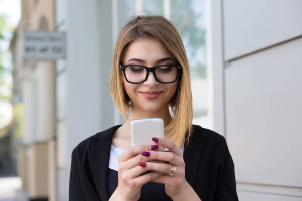 Good news. Woman wearing glasses business black wear jacket dress texting on the smart phone walking in the street in a sunny day office building on background - Zdjęcie, obraz