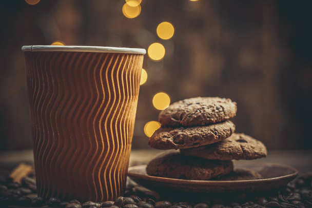 Cups and cups with coffee, coffee grains and gingerbread cookies nearby for refreshments in warm home colors - Photo, Image