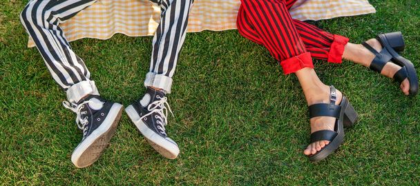 Piernas de dos amigos en pantalones a rayas relajándose en un parque en hierba libre
 - Foto, Imagen