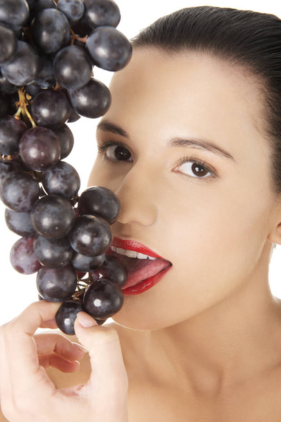 Beautiful sensual brunette eating grapes, isolated on white background  - 写真・画像