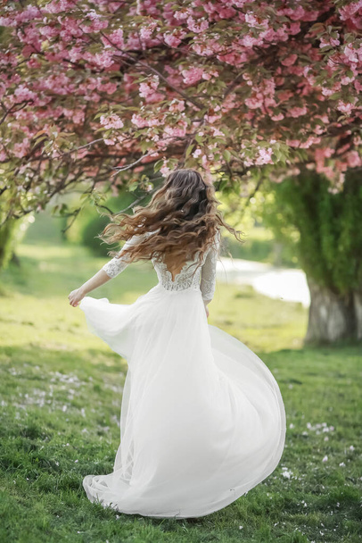 The bride a young woman in a long white dress whirls and dances in a spring Park - Zdjęcie, obraz