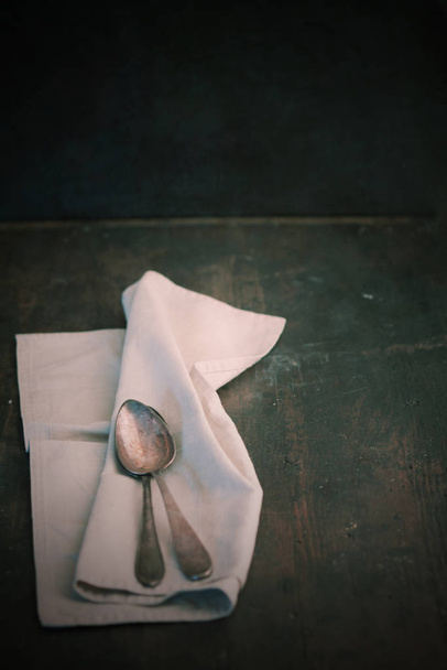 Folded plain white linen napkin and teaspoons on an old dark wooden table with copyspace - Valokuva, kuva