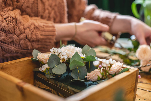 Kobieta kwiaciarnia zbiera kompozycję kwiatową w drewnianym pudełku. Wiosenny bukiet róż w pastelowych kolorach w kwiaciarni - Zdjęcie, obraz