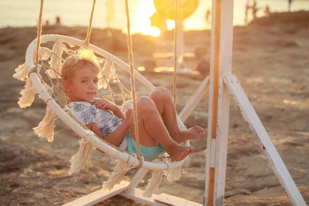 A child at sunset rides in a hanging swing outdoors - Photo, Image